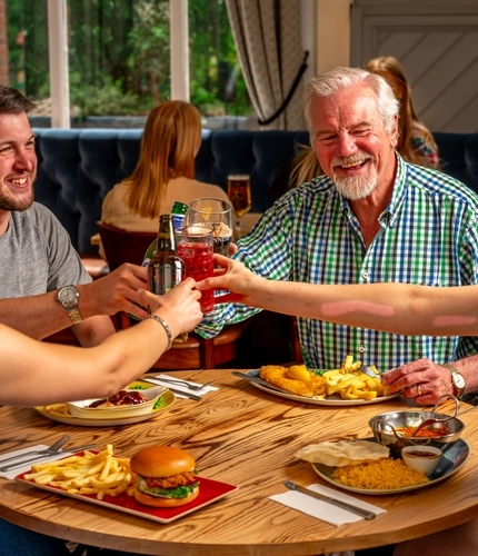 A mixed group of people, seated at an indoor table, holding their drinks in a "Cheers" position.