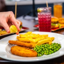 Person squeezing lemon on fish & chips