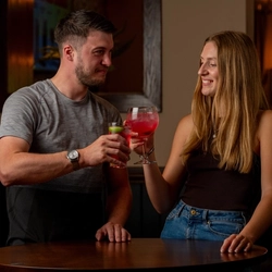 A couple standing at a high table with cocktails in their hands raised in a Cheers type motion.