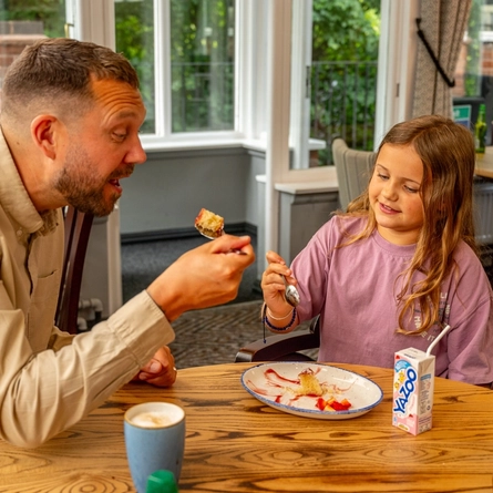 An image of a young girl enjoying a dessert and drink with her father, within the interior restaurant and seating area at a Hungry Horse venue.