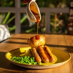 A served main of sausage and mash with a customer pouring gravy available at Hungry Horse venues.