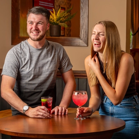 A man and a woman seated at an indoor table enjoying cocktails.